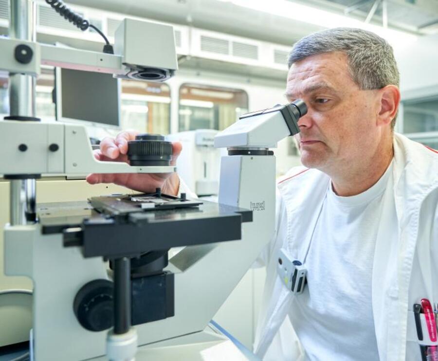 Vědec sedí v laboratoři, dívá se do mikroskopu