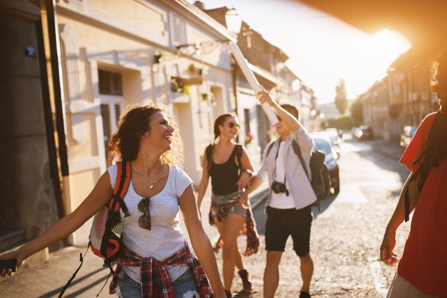 Patru turiști tineri cu rucsacuri merg agale pe strada însorită a unui oraș