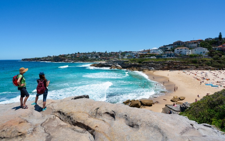 Dos mujeres con sombrero y mochila mirando desde una roca la playa de Tamarama en Australia