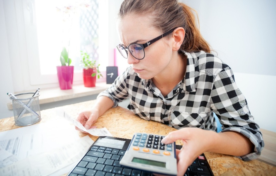 Donna dall'aria stressata seduta a una scrivania con in mano una calcolatrice e uno scontrino
