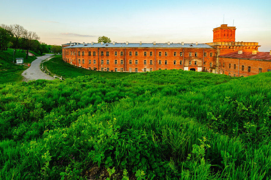 Twierdza Modlin. Widok na koszary otoczone fosą i terenem zielonym.