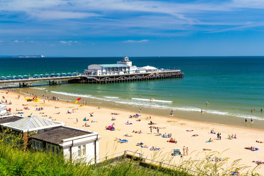 A view of Bournemouth pier and holidaymakers on the sandy beach on a summer day.