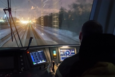 Een machinist zit in zijn cabine aan de knoppen en kijkt ’s nachts door de voorruit naar het spoor