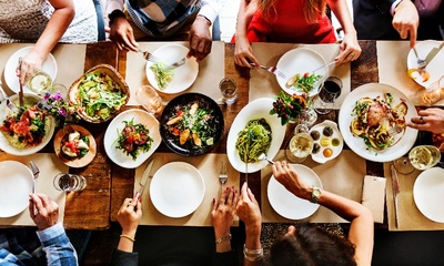 Grupo de personas sentadas en una mesa de madera dispuesta con varios platos de ensalada y pasta de un aspecto delicioso.