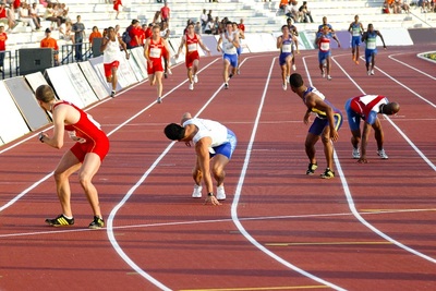 Спортисти се състезават в дисциплината „щафетно бягане“, наблюдавани от публиката на трибуните