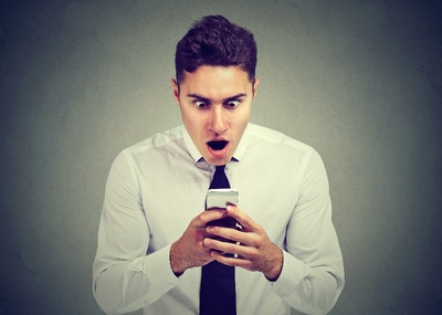 Een jonge man met een hemd en stropdas aan kijkt geschokt naar zijn smartphone